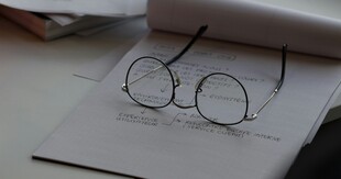 grafika ozdobna, na zdjęciu zapisana kartka papieru i okulary