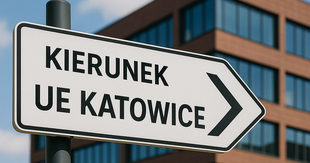 Znak w kształcie strzałki z napisem ‘Kierunek UE Katowice’ i strzałką w prawo, ustawiony na tle nowoczesnego budynku z cegły i dużymi oknami – charakterystyczny gmach A Uniwersytetu Ekonomicznego w Katowicach.